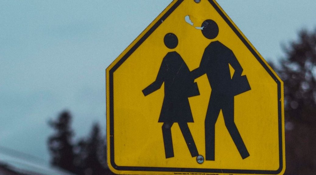 two black figures walk together on a yellow traffic sign