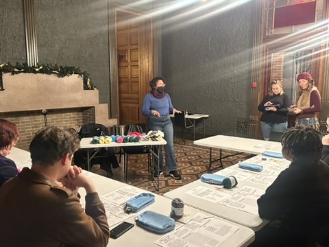 Kristen standing in front of a room teaching people basic crochet